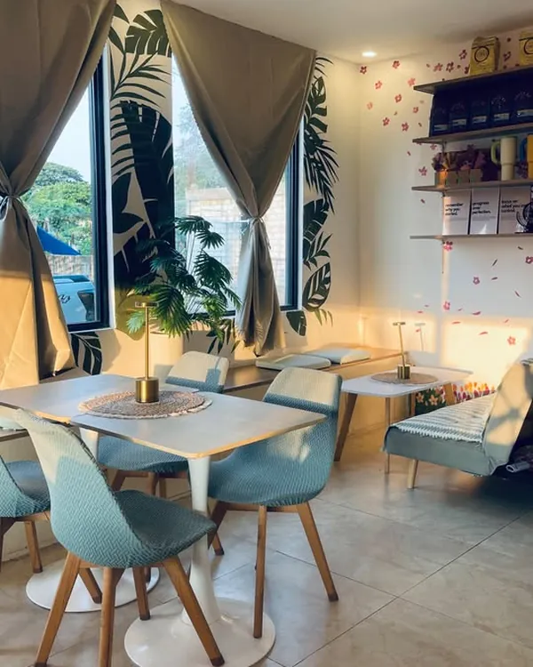 A window table with pale aqua chairs beside a hand-painted palm-leaf mural